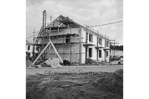Kolberg-Körlin-Straße: Mehrfamilienhäuser: Haus im Rohbau mit Gerüst und Dachsparren: davor Baumaterial: hinten links weiteres Haus im Bau: hinten rechts Wohnhaus