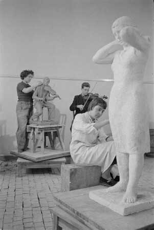Studenten der Bildhauerklasse von Walter Arnold beim Modellieren. Im Vordergrund die Gips-Statue einerstehenden Frau, ein Kopftuch bindend (1960/1962)