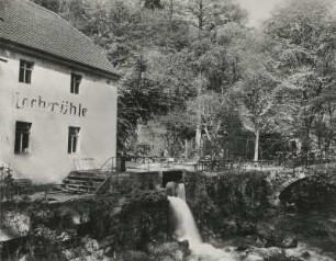 Lohmen-Mühlsdorf. Wohnhaus Gaststätte Lochmühle mit Biergarten. Blick über die Wesenitz mit Überlauf des Mühlgrabens und Fußgängerbrücke