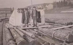 Schwimmendes Floß unweit der Eisenbahn- und Straßenbrücke Bad Schandau. Flößer stehend vor der mit Plane bespannten Floßbude : Elbsandsteingebirge. Schwimmendes Floß unweit der Eisenbahn- und Straßenbrücke Bad Schandau. Flößer stehend vor der mit Plane bespannten Floßbude