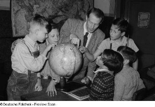 Porträt eines Lehrers mit Schülern an einem Globus