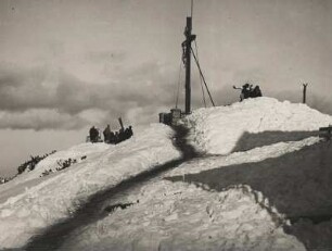 Winter in Oberbayern. Gipfelkreuz des Wank (1.780 m), einem Berg im Südwesten des Elstergebirges. Eine Gruppe von Skifahrern hält sic auf dem Gipfel auf