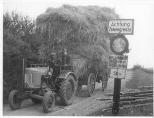 Einbringen der Ernte im Grenzbereich. Traktor mit getreidebeladenem Hänger