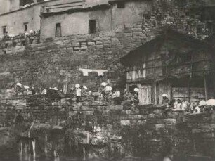 China. Tschungking (Chongqing) am mittleren Jangtse. Stadtbild am Flußufer mit terrassenförmigen Steinmauern und Wohnhäusern. Zuschauer bei einem Bootsrennen