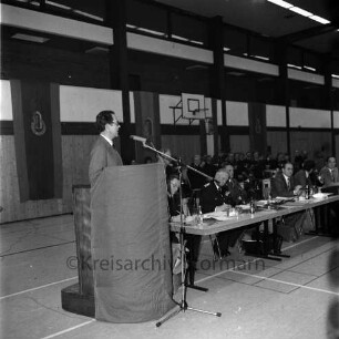 Kreisfeuerwehrverband: Mitgliederversammlung: Reinfeld: Sporthalle des Schulverbands, Schützenstraße: Bürgermeister von Reinfeld Michael Sachse hält Ansprache am Rednerpult: am Tisch Vertreter der Verbandsspitze, des Kreises Stormarn und der Stadt Reinfeld: darunter Landrat Hans-Henning Becker-Birck, Kreispräsident Hubert Priemel, Kreisbrandmeister Heinz Poschmann, Geschäftsführer Heinrich Dittmer, Bürgervorsteher von Reinfeld Claus Slama, dahinter Musikzug der Freiwilligen Feuerwehr Reinfeld, 28. Dezember 1979