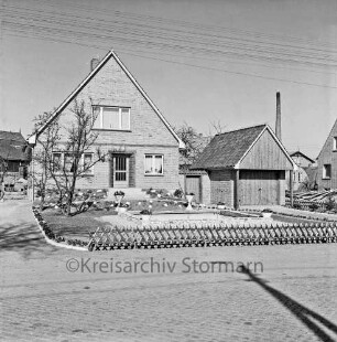 Neubausiedlung: Einfamilienhaus mit Garage: davor geschmückter Vorgarten: links Baum