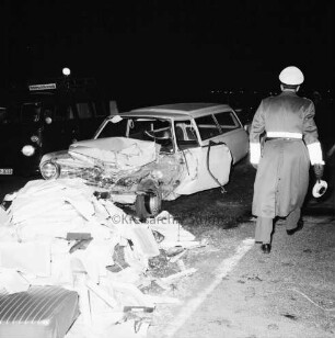 B 404: bei Tralau: Verkehrsunfall: Zusammenstoß von Pkw-Kombi mit Lkw: Pkw-Kombi mit eingedrückter Front: davor auf Fahrbahn Autositz, zahlreiche Pakete von Ladung: rechts Polizist mit Kelle [Rückenansicht]: links Einsatzwagen von Unfallkommando: im Dunkeln, 12. Januar 1965