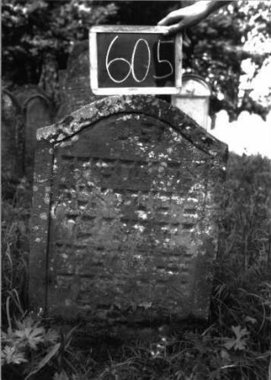 Grabstein 605 (Index: 100105036) Material: Sandstein Zustand: stark verwittert, eingesunken, teilweiser Textverlust Maße HxBxT: 81x52x9 cm Beschreibung: Stele, Konvexbogenabschluss, Schriftfeld durch Rille abgeteilt: Grabstein 605