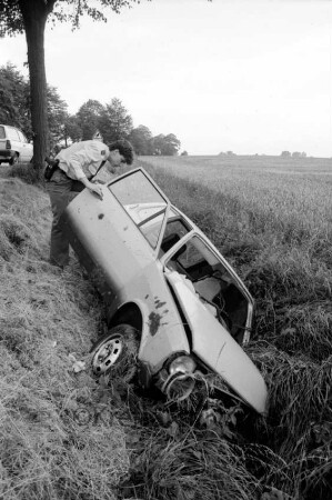 Verkehrsunfall: Hamburger Chaussee: verunglückter Pkw in Graben: links an Tür Polizist: links Straße mit Pkw und Baum: rechts Feld