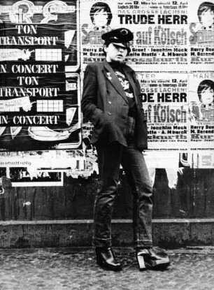 Frau mit Schirmmütze vor Plakatwand