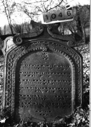 Grabstein 1046 (Index: 99751157) Material: Sandstein Zustand: gut Maße HxBxT: 111x86x14 cm Beschreibung: Stele, Segmentbogenabschluß mit Aufsatz in Sonderform, Schriftfeld eingetieft Symbolik: geometrische Friese, Voluten: Grabstein 1046