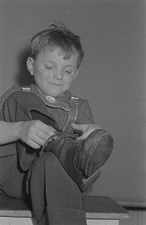 Ein Junge (Lothar) schnürt sich die Stiefel