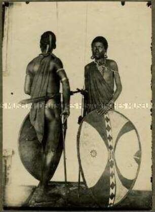 Zwei Massai mit traditionellen Waffen in Vorder- und Hinteransicht