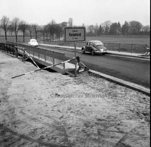 Trave: Brückenneubau: Spannbetonbrücke nach Fertigstellung: links alte Holzbrücke: im Vordergrund Straßenschild Richtung Reinfeld und zwei VW-Käfer: hinten Bäume