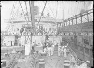 Zahlreiche Passagiere auf der Kapitänsbrücke und beschäftigte Matrosen an Deck des Hochseepassagierdampfers "Bremen", Anlegemanöver im Hafen von New York