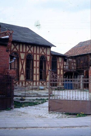 Blick in einen Hof; schmiedeeisernes Tor, Gebäude mit hohen, rundbogigen Fenstern, vermutlich Tanzsaal einer Gastwirtschaft