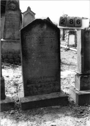 Grabstein 286 (Index: 99797820) Material: Sandstein, weiß Zustand: stark verwittert Maße HxBxT: 96x44x10 cm Beschreibung: Stele, giebelartiger Abschluß oben abgeflacht, Sockel: Grabstein 286
