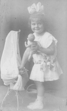 Album mit Porträtserie eines kleinen Mädchens. Mädchen im Sommerkleid, neben einem Puppenbett stehend und eine Puppe haltend
