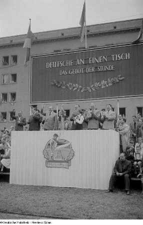 Blick auf die Tribüne mit Otto Grotewohl (3.v.l.), Erich Uhlich (3.v.r.), Max Reimann (2.v.r.) und Paul Fröhlich (rechts) auf der Straße der III. Weltfestspiele (heutige Jahnallee)