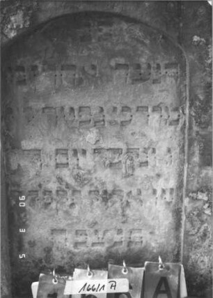 Grabstein 166/1 (Index: 99608851) Material: Sandstein Zustand: stärker verwittert Maße HxBxT: 112x61x11 cm Beschreibung: Stele, geschwungener Abschluß, Schriftfeld eingetieft mit Segmentbogenabschluß Besonderheit: Daten fraglich!: Grabstein 166/1A