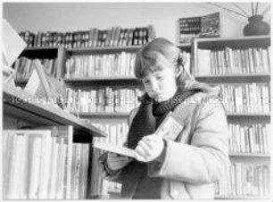 Mädchen liest Buch in einer Bibliothek (Altersgruppe bis 14)