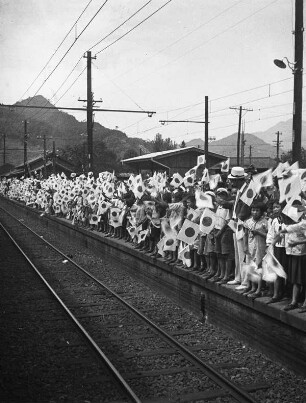 Honshū. Präfektur Yamanashi. Bahnstation zweischen Fujiyoshita und Otsuki. "Ein Kamerad zieht ins Feld". Kinder und Erwachsenen am Bahnsteig, die Flagge Japans (Nisshōki bzw. Hi no Maru) schwenkend