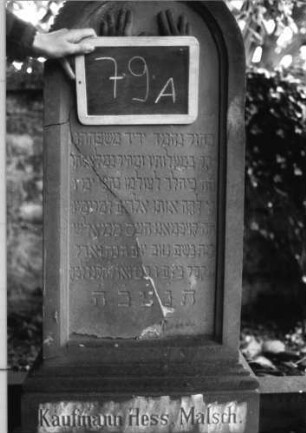 Grabstein 79 (Index: 100080579) Material: Sandstein Zustand: Stele mehrfach gesprungen Maße HxBxT: 143x43x20 cm Beschreibung: unterer Sockelteil rustica, Rundbogenabschl. mit Mittelakroter, Schrift eingetieft Symbolik: segnende Hände, Blätter mit Akroter Steinmetz: P. Müller: Grabstein 79A