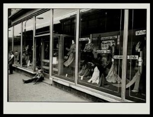 Schaufenster eines Modegeschäfts an der Schönhauser Allee mit zwei Kindern, die vor dem Eingang sitzen, Prenzlauer Berg, Berlin