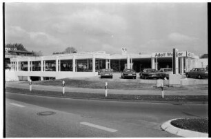 BMW-Niederlassung Adolf Werner: Ostring, Ecke Beimoorweg: Neueröffnung Anbau: Außenansicht: Ausstellungsraum Erdgeschoss, links darunter Tiefebene: rechts Altbau mit Firmenname: davor Außenfläche, Autor, Stele mit Firmenlogo