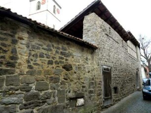 Kirchhofmauer im Südosten über Ortsseite mit unterschiedelichen Erhaltungszuständen - Mittelteil mit Wehrgang und Steinbrüstung sowie vereinfachtem Pultdach des innen angebauten Gaden