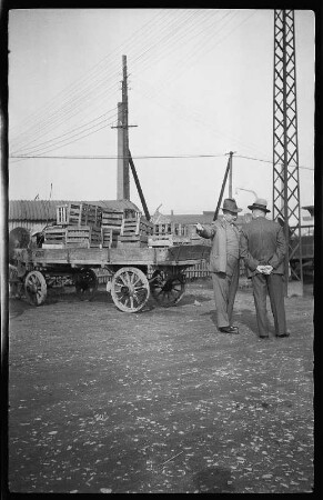 Händler im Gespräch auf dem Gelände der Großmarkthalle Leipzig, im Hintergrund ein Leiterwagen mit leeren Holzkisten