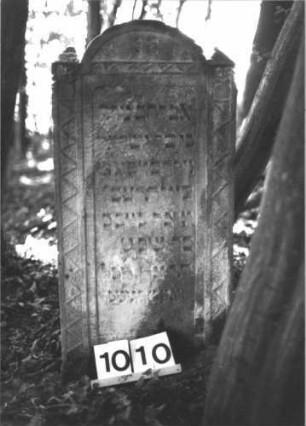 Grabstein 1010 (Index: 99899585) Material: Sandstein Zustand: verwittert Maße HxBxT: 94x46x11 cm Beschreibung: Stele mit eingezogenem Rundbogenabschluss, Einzüge pyramidenförmig erhöht, umlaufender Rahmen mit Zackenfries Symbolik: Zackenfries Besonderheit: Kindergrab: Grabstein 1010
