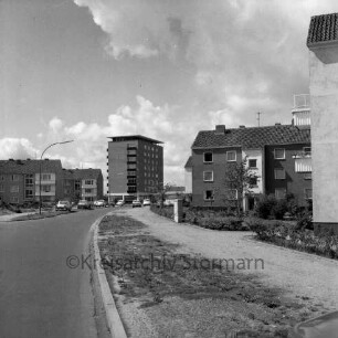 Stonsdorfer Weg: mittig parkende Pkws, Wohngebäude an den Seiten, im Hintergrund das Rathausgebäude: Blick Richtung Westen