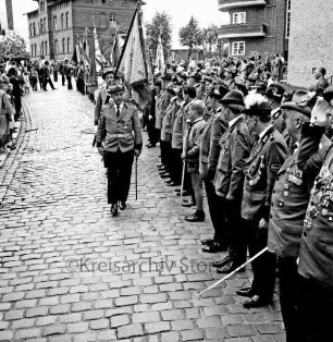 Schützenfest: Veranstalter Bürgerschützengilde von 1627 e.V. Bad Oldesloe: Umzug: Bahnhofstraße: Fahnenträger beim Vorbeimarsch an angetretenen Abordnungen der Schützenvereine: links am Straßenrand Zuschauer, 25. Juli 1965