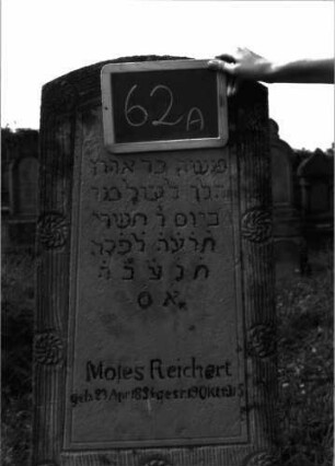Grabstein 62 (Index: 100100751) Material: Sandstein, unterer Sockel Kalkstein Zustand: verwittert Maße HxBxT: 150x49x20 cm Beschreibung: konische Stele, getreppter Sockel, oberer Sockelteil rusticaartig Symbolik: Blüten um das Schriftfeld: Grabstein 62A
