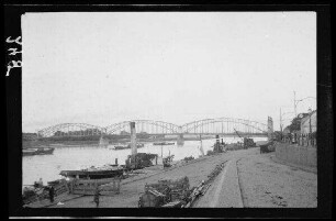 Uferbefestigung an einem Fluss mit Brücke aus geschwungenen Stahlträgern und Betonsockeln