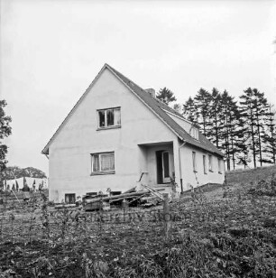 Rentnerwohnheim: ehemaliges "Jägerhaus": vorn Zaun und Bretterstapel: hinten links Frau vor Wäsche auf der Leine: hinten rechts Tannen