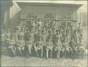 46 Offiziere in Uniform mit Mütze oder Pickelhaube, teils stehend, teils sitzend vor Gebäude in Warschau