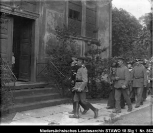 Arbeiter Wilhelm Lampe aus Wolfenbüttel, Johannisstr.1, als Sergeant des alten Braunschweigischen Infanterieregiments Enthält: Lampe wird von einem Soldaten zu einem Hauseingang geführt, dahinter: Soldaten mit Damen, paarweise gehend