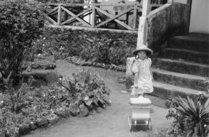 Mädchen mit Puppenwagen : Ein Mädchen mit Puppenwagen auf einem Gartenweg vor einer Villa.