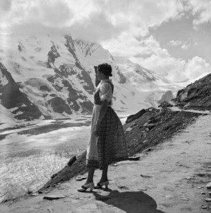 Frau im Dirndl blickt oberhalb eines Gletschers stehend Alpengipfel