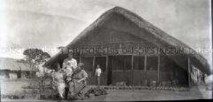 Gruppenbild zweier sitzender Farmerfrauen und eines Farmers mit Baby vor einem Haus