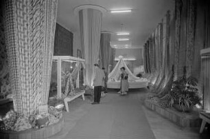 Besucher der Leipziger Herbstmesse 1955 betrachten drapierte Stoffbahnen