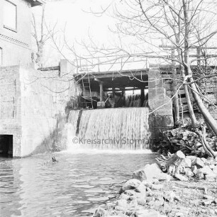 Mühlenwehr zwischen Mühlenteich und Glinder Au: darüber baufällige Brücke der Mühlenstraße: rechts Bäume: links Mühlengebäude