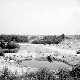 Kiesgrube: Blick von oben in die Grube: vorn Baggersee: rechts Lkw: im Hintergrund Hänge der Grube mit Büschen