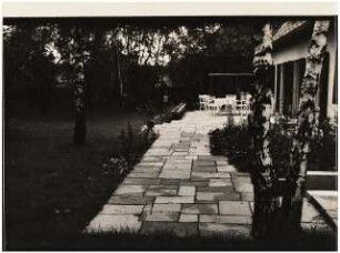 Wohnhaus und Garten [noch nicht indentifiziert]: Terrasse mit Plattenverlegung, weiße Sitzgruppe evt. Klappstühle im Hintergrund, vorne Birke
