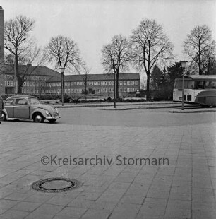 Haupthaus [später Gebäude A]: Mommsenstraße: in der Mitte Anbau mit Garagentrakt: davor Innenhof und Bäume: vorn Bahnhofsvorplatz mit Busbahnhof, Bus VW-Käfer