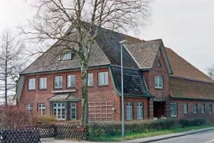 Hauptstraße 37: traufständiges Bauernhaus aus Backstein: Straßenfront, rechts Wirtschaftstrakt, Bildmitte Wohntrakt, Risalit mit Dreiecksgiebel und Eingangsloggia: Giebelseite Wohntrakt, Auslucht, Rankgitter: davor Gartenhecke