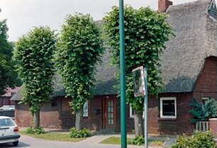 Reinbeker Straße 1: traufständige Backsteinkate mit Reetdach: Straßenfront: rechts Wohntrakt mit Eingangstür, links Wirtschaftstrakt: davor drei Lindenbäume