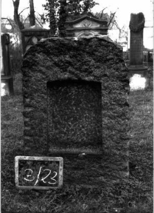 Grabstein 86 (Index: 99804729) Material: Granit Zustand: Platte fehlt Maße HxBxT: 93x60x34 cm Beschreibung: grob stelenförmig behauener Stein, eingetieftes Schriftfeld mit Segmentbogen: Grabstein 3/23